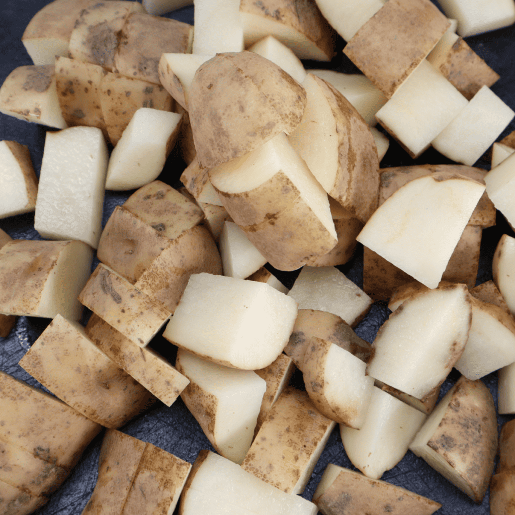Washing, drying, and dicing potatoes into small quarters on a cutting board for air fryer cheesy ranch potatoes recipe