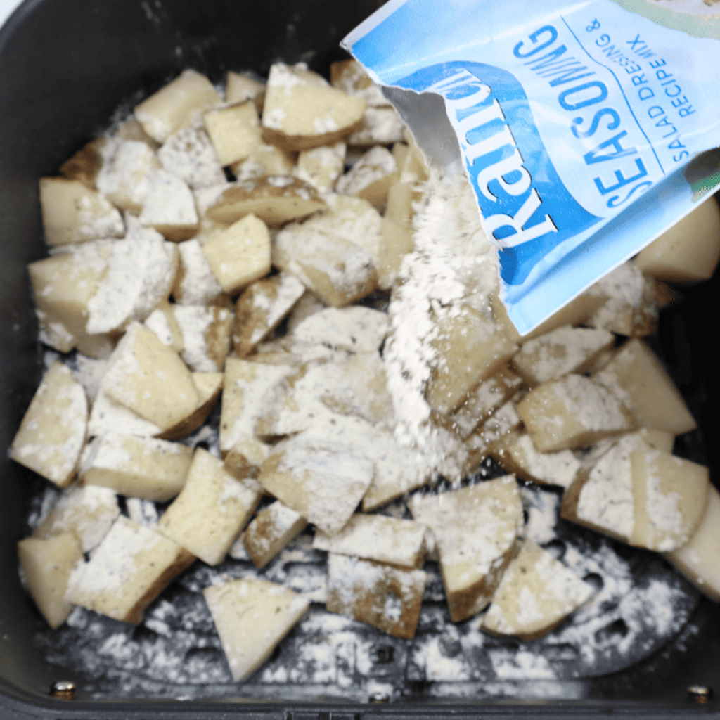Tossing diced potatoes with olive oil and ranch seasoning in the air fryer basket, topped with diced bacon before cooking