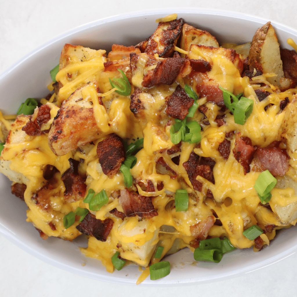 Golden crispy air fryer ranch potatoes topped with melted cheese and bacon, served on a white plate