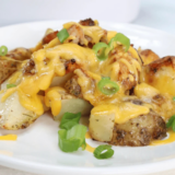 Golden air fryer cheesy ranch potatoes topped with melted cheese and sprinkled with herbs, served in a white bowl