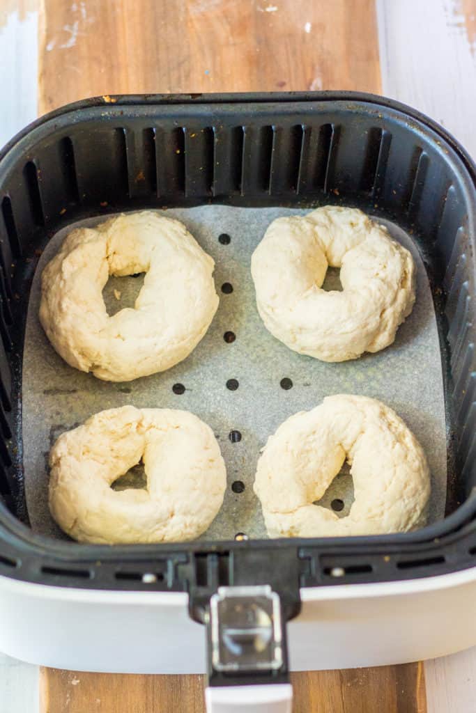 Raw gluten-free everything bagels arranged in an air fryer basket before cooking.