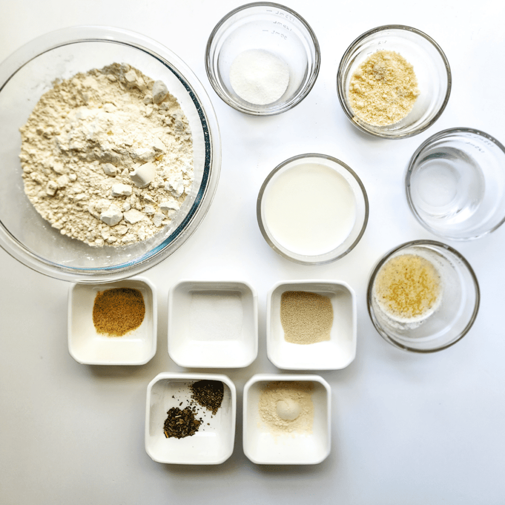 Image of ingredients for making Domino's Parmesan Bites including yeast, sugar, oil, milk, bread flour, and garlic Parmesan topping components such as garlic powder, parsley, salted butter, and grated Parmesan cheese.