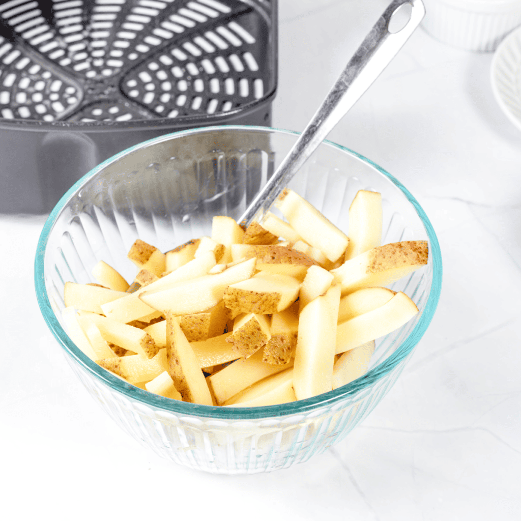Preheat air fryer, wash and scrub Russet potatoes, peel if desired, cut into 1/2 inch thick fries for even cooking.