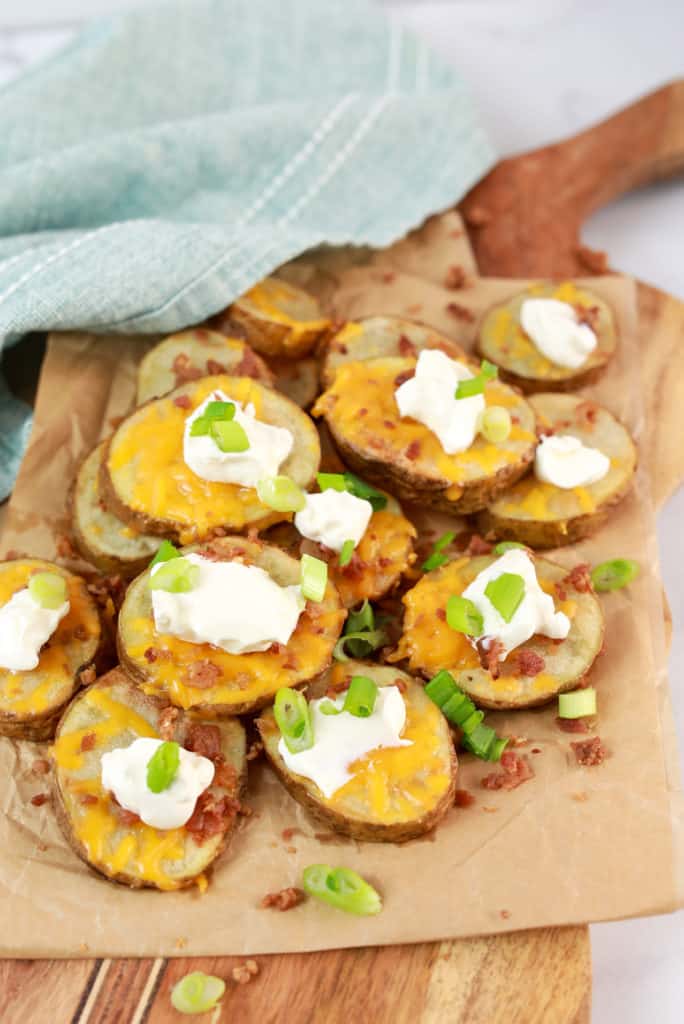 Golden air fryer potatoes topped with melted cheese and chopped green onions on a white plate.