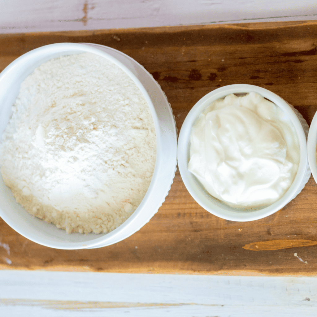 Ingredients for air fryer gluten-free everything bagels including Greek yogurt, gluten-free flour, baking powder and everything bagel seasoning on a cutting board]