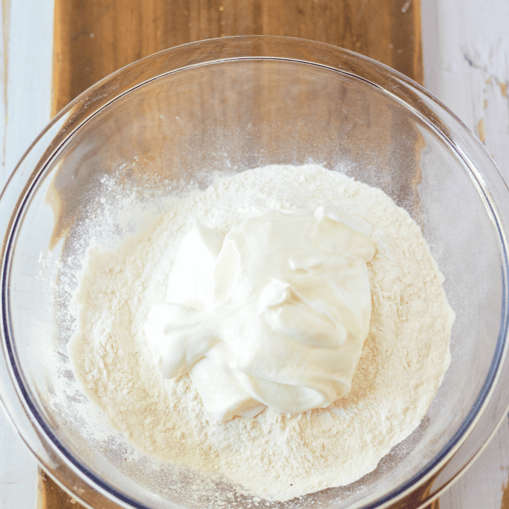 Gluten-free bagel dough being mixed with Greek yogurt in a glass bowl with a wooden spoon.