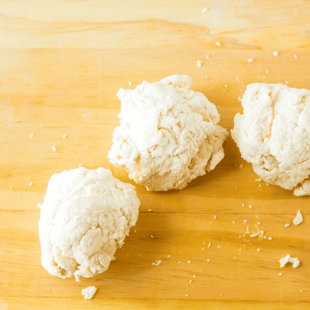 Four shaped raw gluten-free bagels with center holes formed on a piece of parchment paper.