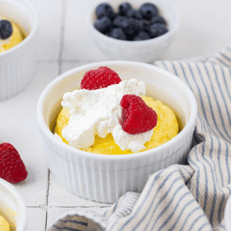 Golden, fluffy air fryer soufflé pancakes in ramekins topped with whipped cream and fresh berries.