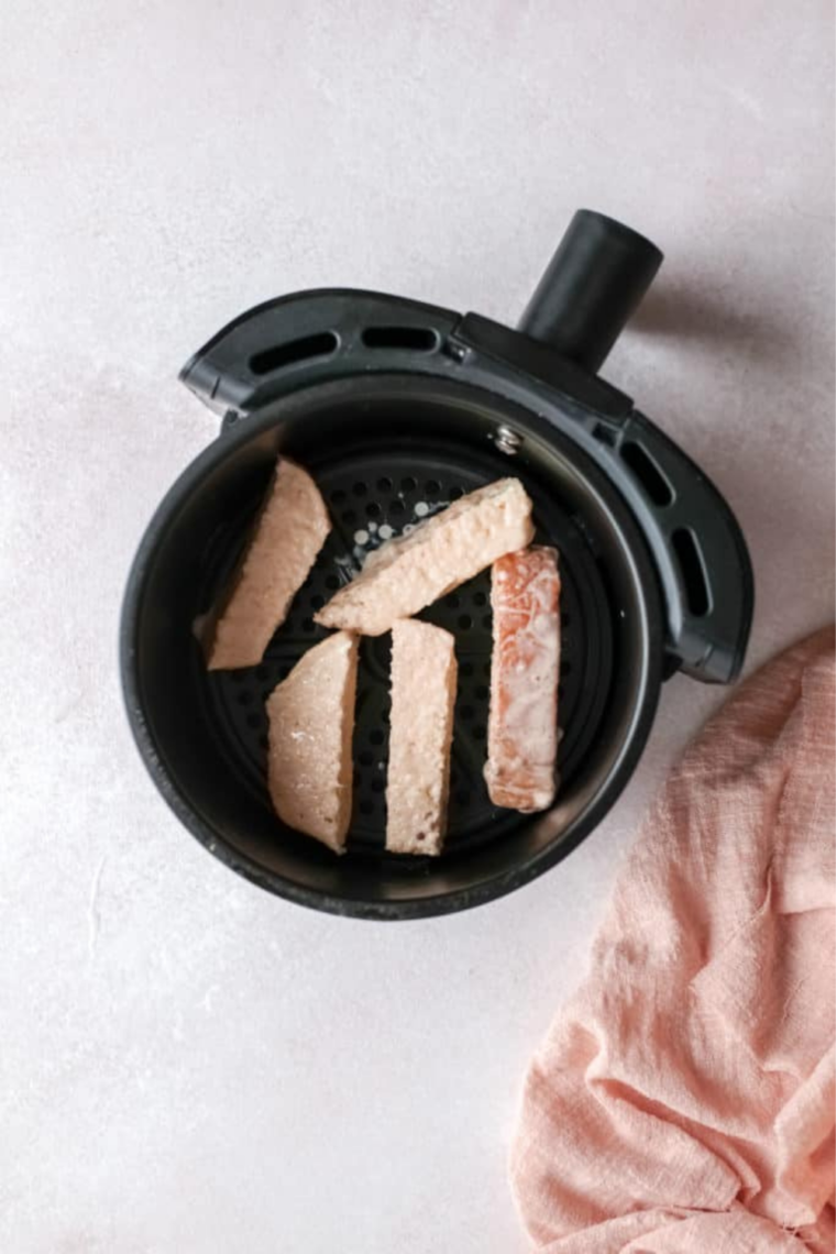 Arranging French toast sticks in the air fryer basket and spraying with cooking spray before cooking.