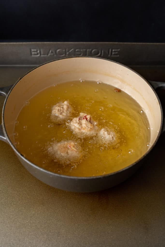 Carefully shaping dough into a round ball and placing it into hot oil for frying.