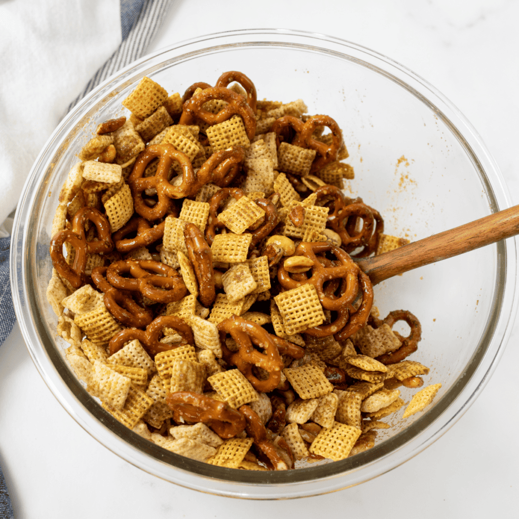 Pouring seasoned butter over the Chex mixture and stirring to coat evenly
