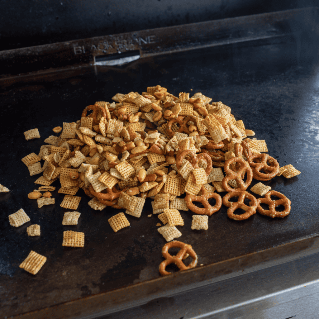 Chex party mix spread in an even layer on a preheated Blackstone griddle