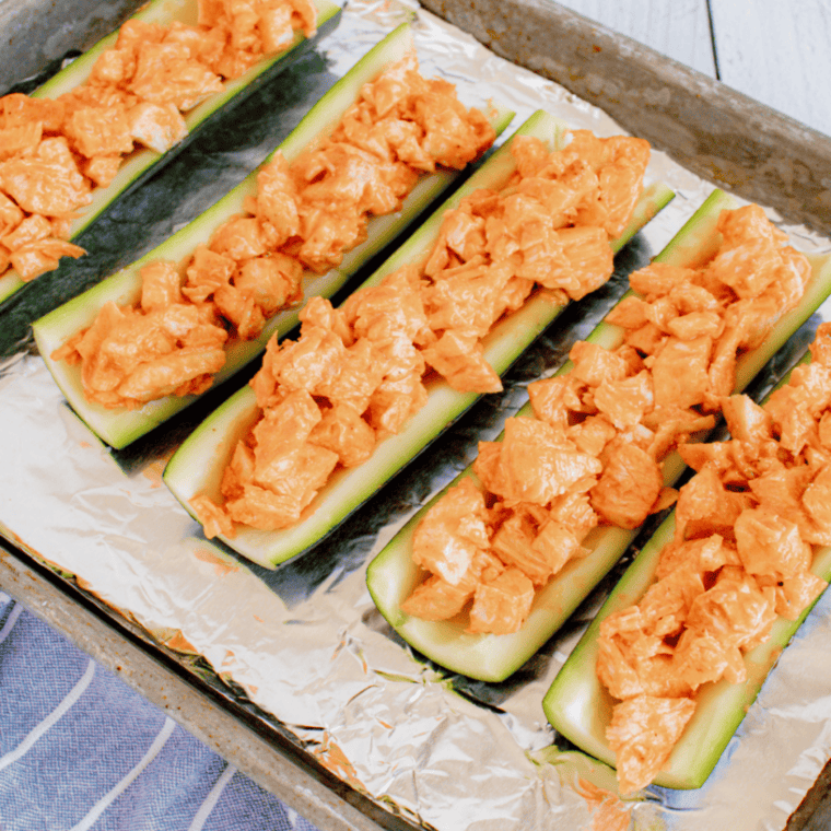 Mixing shredded chicken with Buffalo sauce in a bowl for zucchini boats.