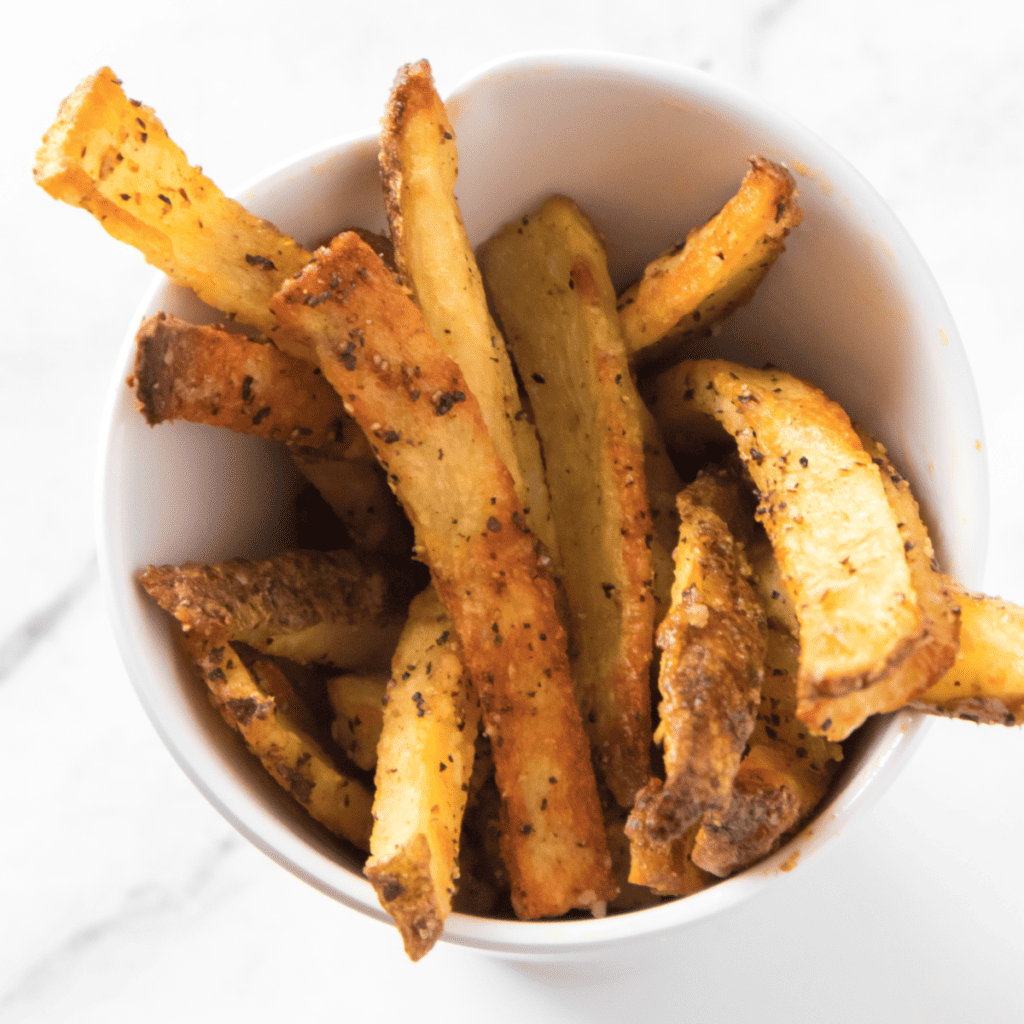Freshly made Copycat Five Guys Cajun Fries on a wooden cutting board, garnished with fresh herbs.