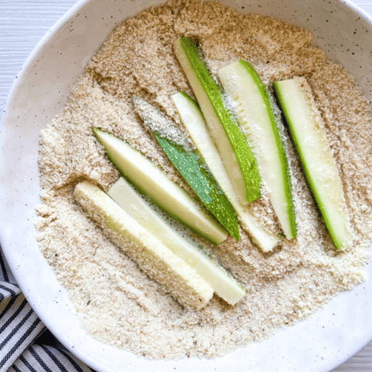 Coat zucchini pieces in milk, then roll in flour mixture for even breading.