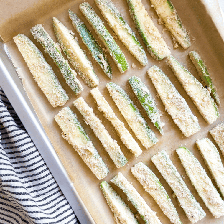 Golden brown and crispy baked zucchini pieces on a baking sheet, flipped halfway through for even cooking.