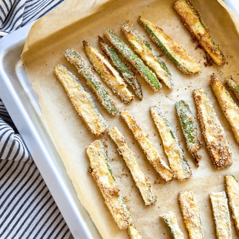Golden brown baked zucchini fries on a parchment-lined baking sheet, crisp and ready to enjoy.
