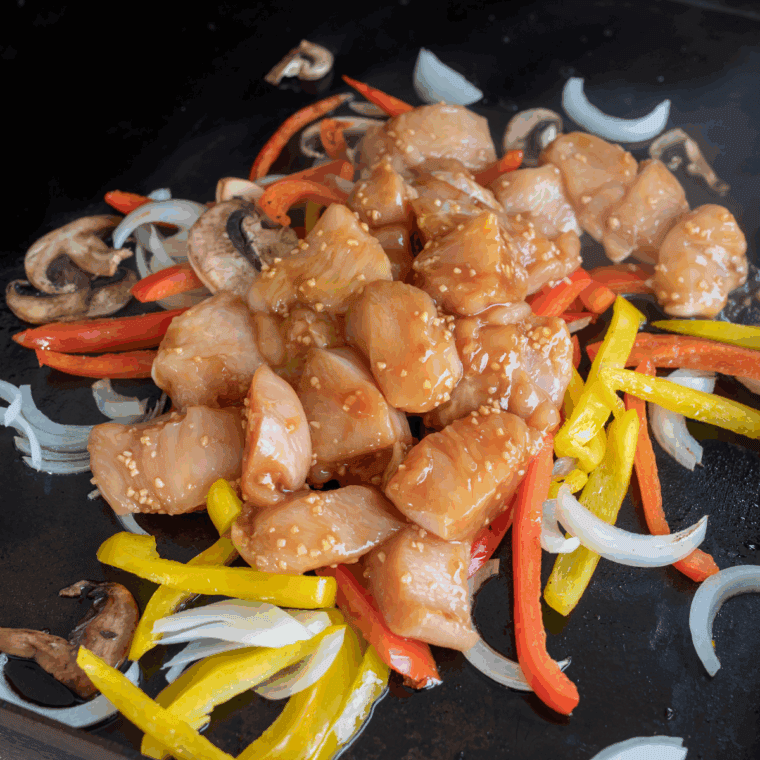Seasoned chicken pieces searing in a single layer on the Blackstone griddle