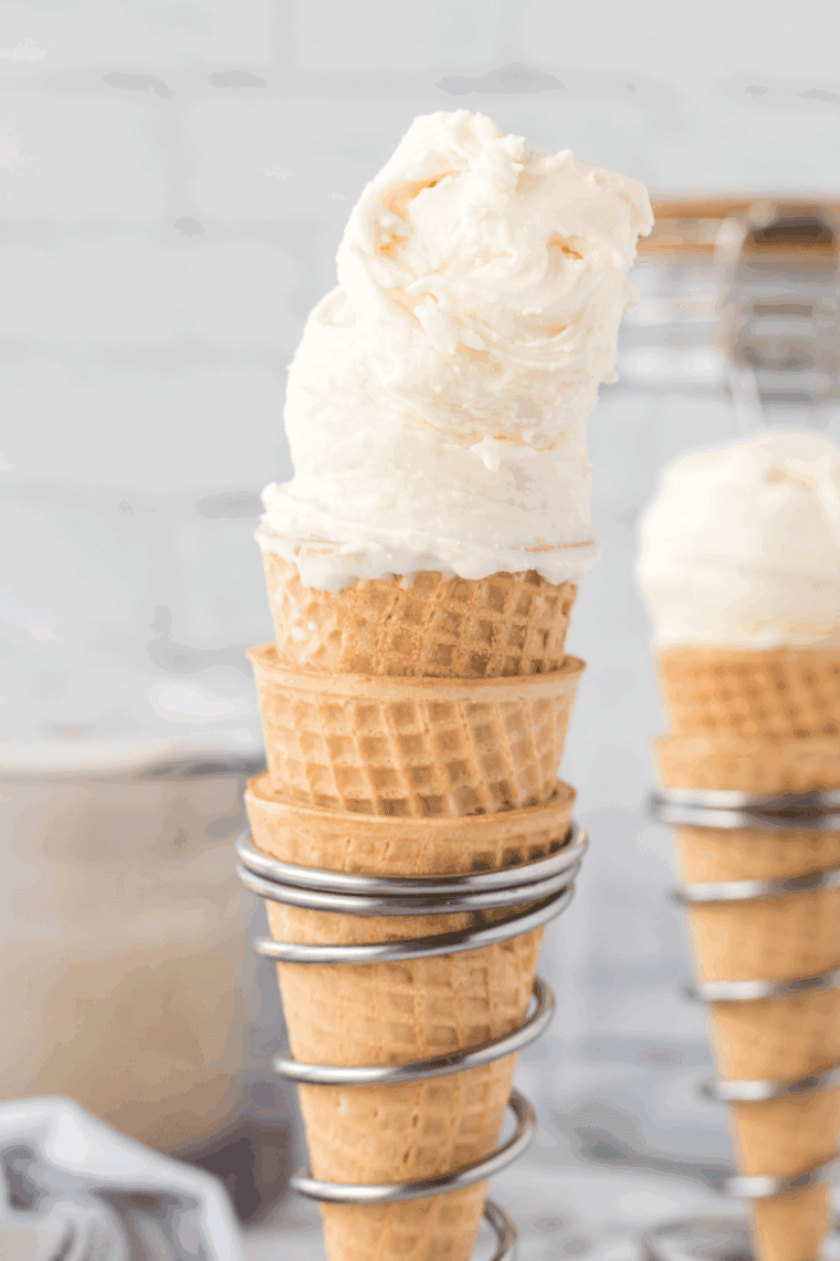 Two scoops of homemade Ninja Creami vanilla bean ice cream in a waffle cone, showing its creamy speckled texture
