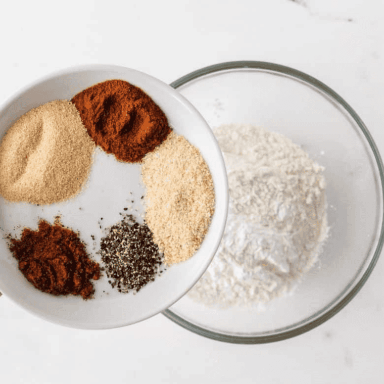 Mixing flour, cornstarch, paprika, garlic powder, onion powder, red pepper, black pepper, and salt to make Cajun spice blend.