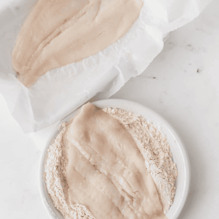 Rubbing olive oil on flounder fillets and coating with Cajun flour mix, pressing firmly to ensure coating sticks.