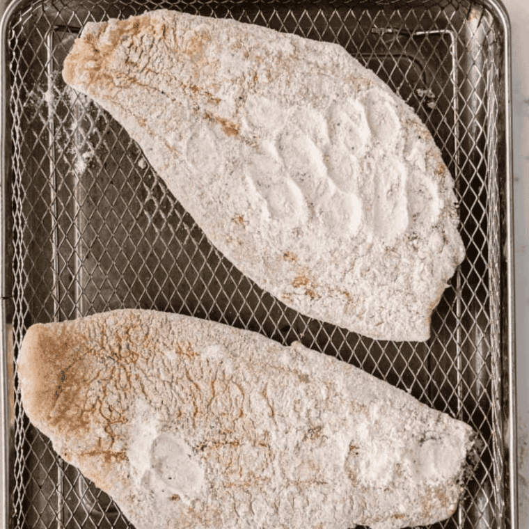 Spraying air fryer basket and coated flounder fillets with cooking spray, then air frying at 400°F for golden brown results.
