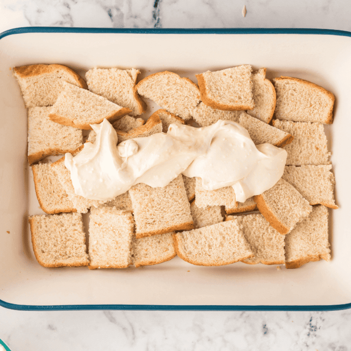 Pouring custard over cubed bread in a baking dish for air fryer French toast casserole