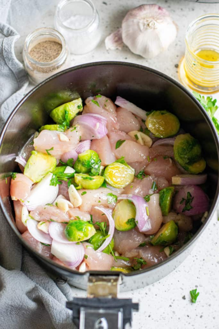 Bowl filled with chicken, Brussels sprouts, onions, garlic, honey, oil, and seasonings being mixed together