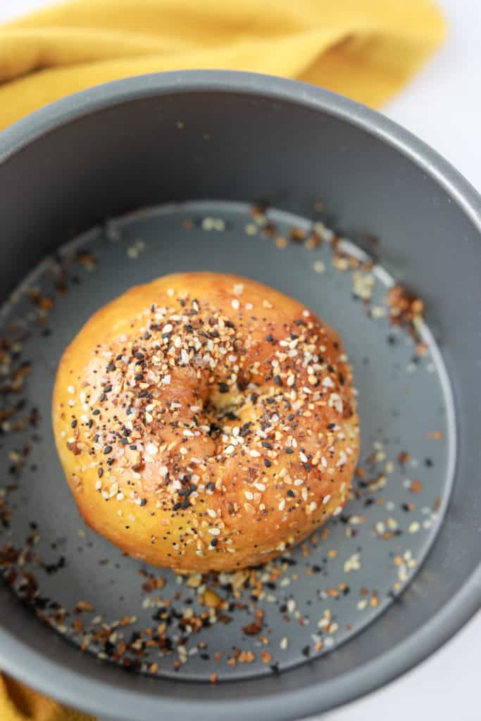 Golden brown gluten-free everything bagels in the air fryer basket after cooking with crispy seasoning topping.