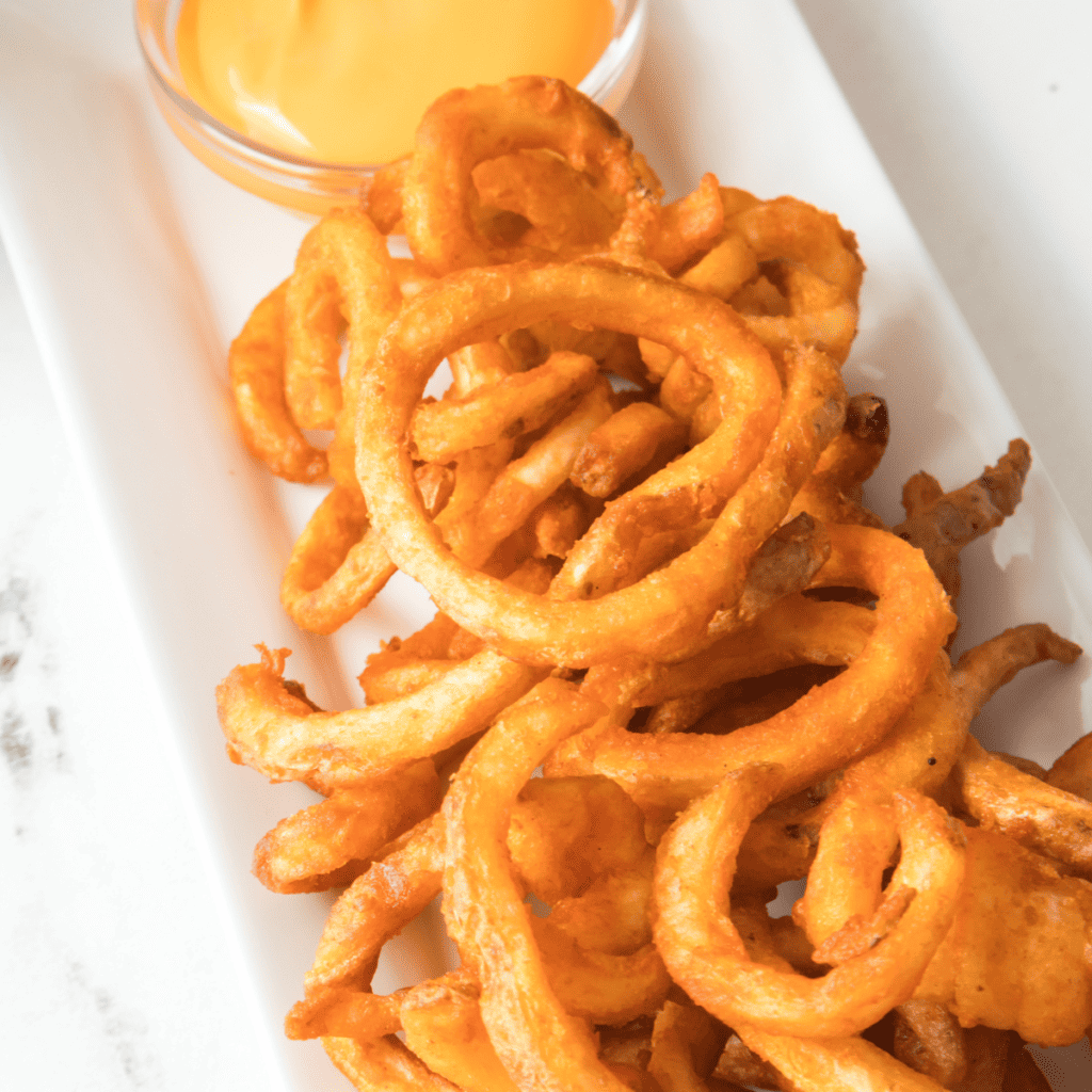 Plate of Arby's Curly Fries In Air Fryer on table with dipping sauce.