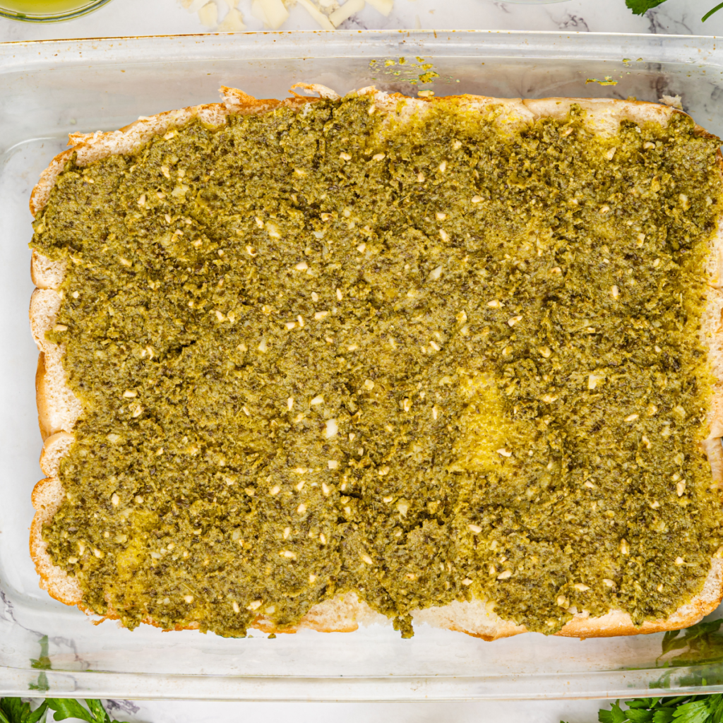 Layering basil pesto, shredded rotisserie chicken, and melted mozzarella cheese on the bottom half of slider rolls inside an air fryer basket.