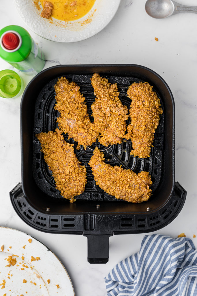 Crispy chicken fingers placed in air fryer basket.