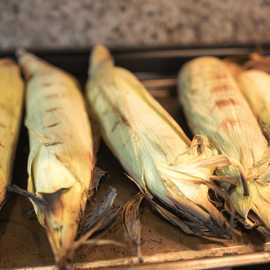 Plate of Air Fryer Corn On The Cob In Husk on kitchen cutting board.