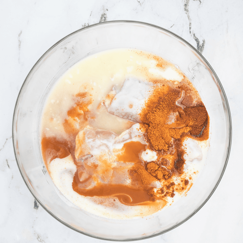 Chicken thighs marinating in a large bowl with hot sauce, pickle juice, cayenne pepper, paprika, onion powder, garlic powder, and buttermilk for a flavorful infusion.