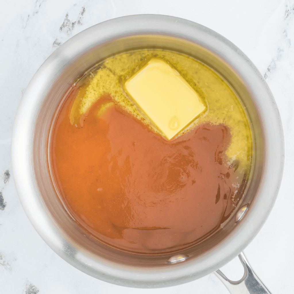 Small saucepan on the stove with butter, honey, and hot sauce being stirred together to make a hot honey sauce.