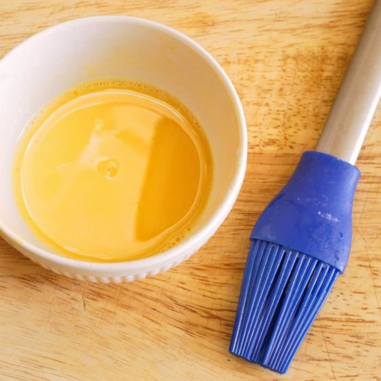 Whisking an egg with water in a small bowl to create an egg wash for coating zucchini slices.