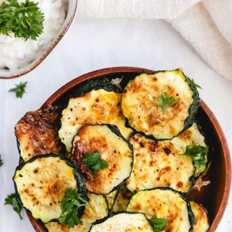 Golden, crispy zucchini chips seasoned with Cool Ranch spices, freshly made in the air fryer and served on a plate.