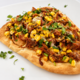 Slice of air fryer street corn carnitas flatbread topped with avocado and cotija