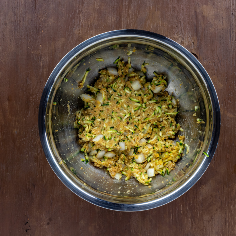 mixing zucchini onion garlic breadcrumbs egg and spices into thick veggie burger mixture by hand in bowl