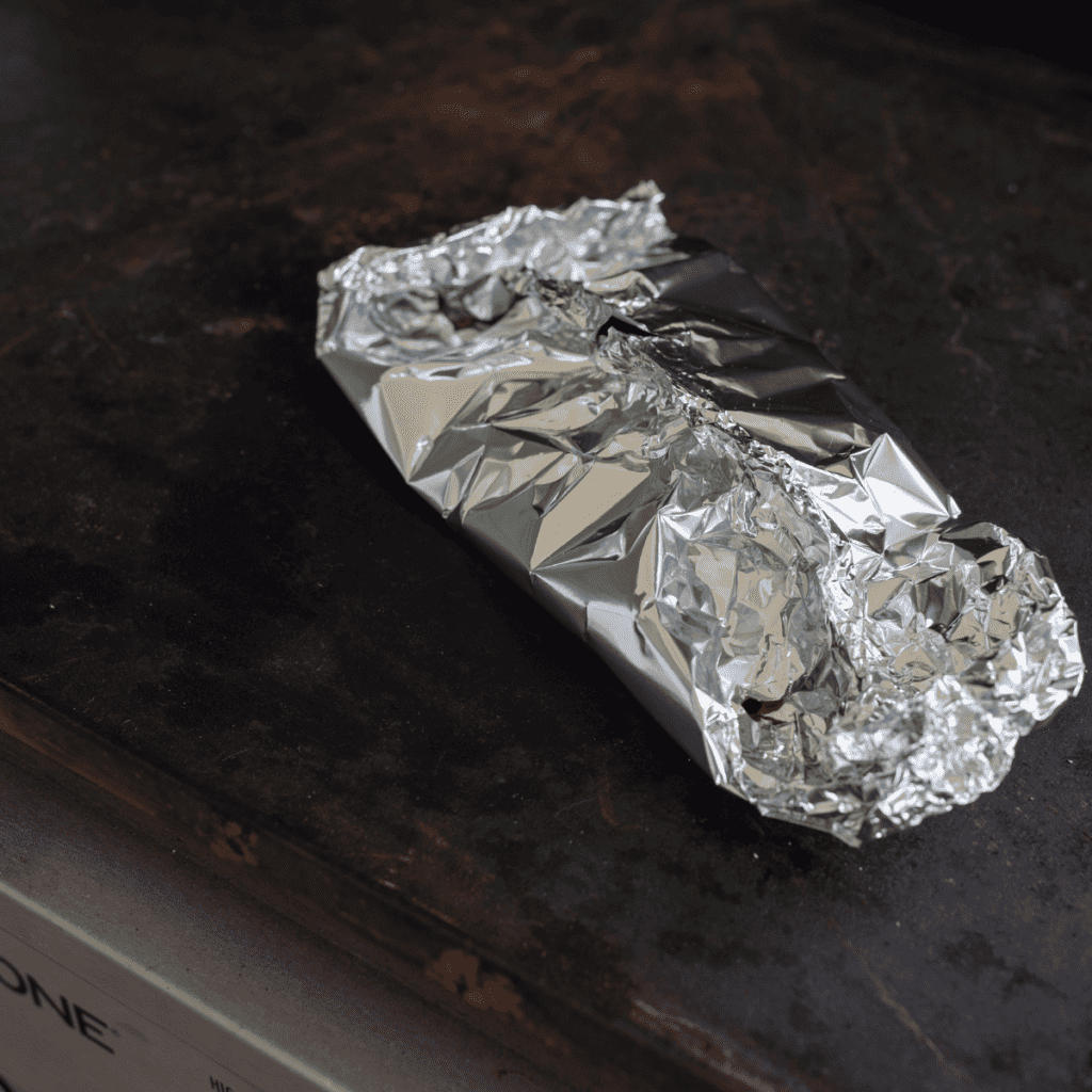 Apple cobbler filling and crumb topping wrapped in foil packets and placed on a Blackstone griddle for cooking.