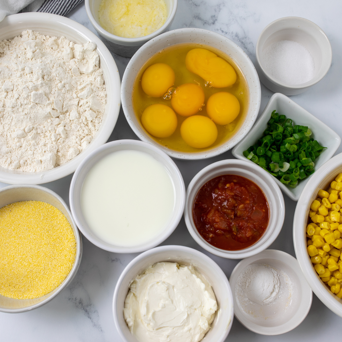 Corn cake ingredients laid out: cornmeal, flour, eggs, buttermilk, corn kernels, butter and green onions