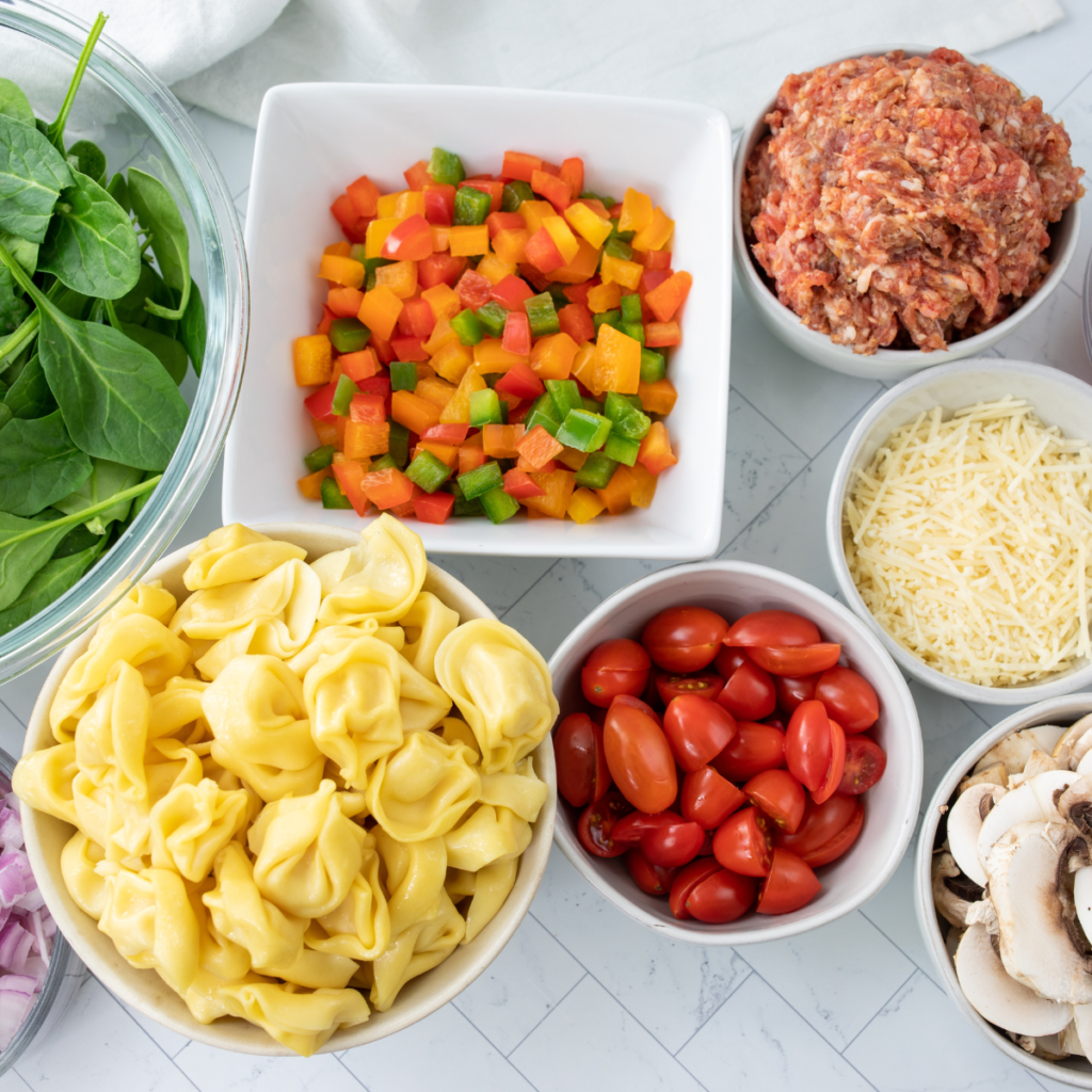 Ingredients for Blackstone Italian sausage tortellini laid out on a wood board.
