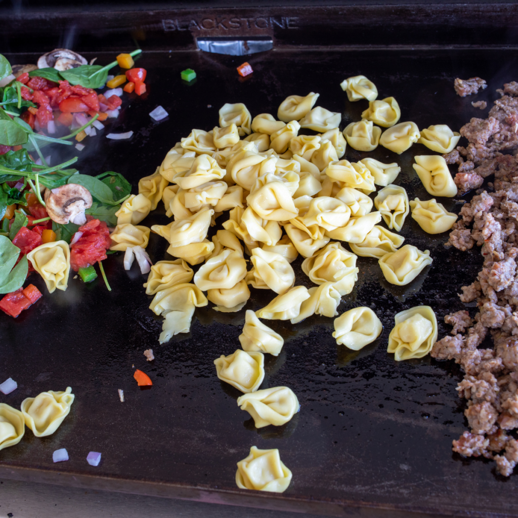 Bell peppers, onions, and mushrooms sautéing on a Blackstone griddle.