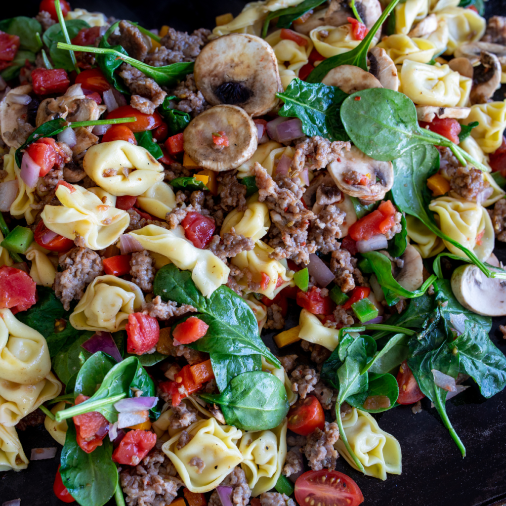 Creamy tortellini and browned Italian sausage cooking on a Blackstone griddle
