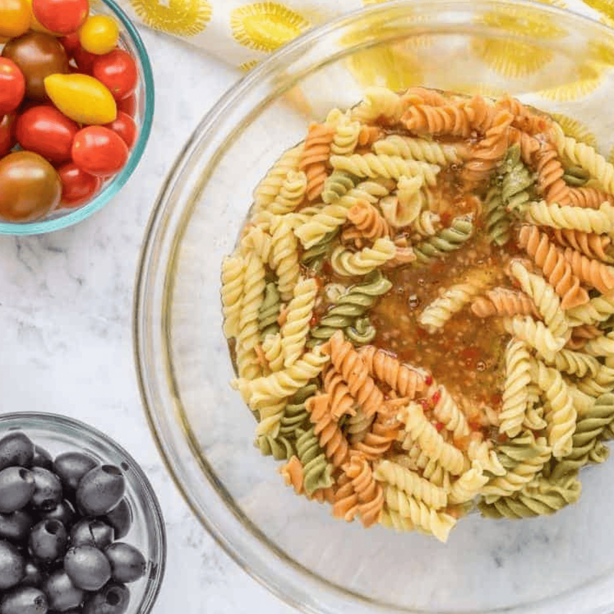 Al dente rotini pasta mixed with dressing in a large bowl after rinsing with cool water.