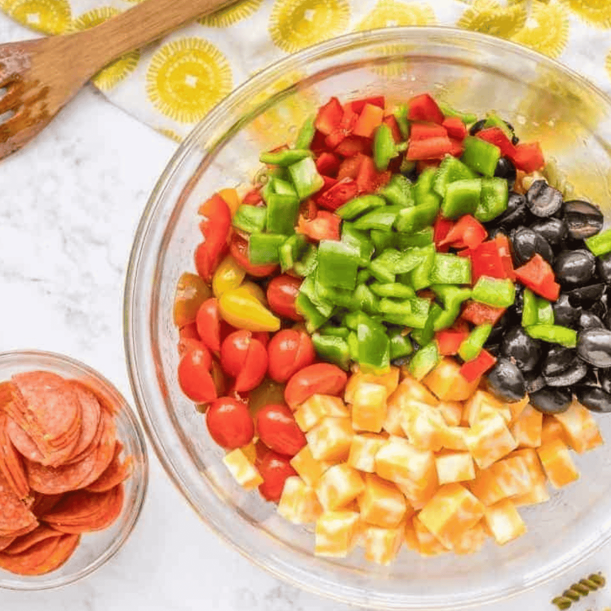 Chopped red bell peppers, various colored bell peppers, red onion, black olives, and tomatoes in a bowl.
