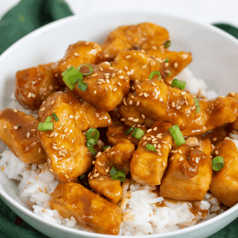 Crispy honey sesame chicken bites coated in sticky glaze, served on a plate.