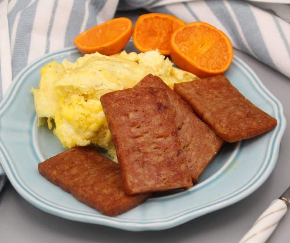 SPAM cooked in air fryer on a plate with scrambled eggs and oranges