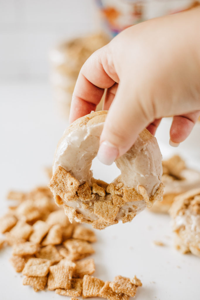 Crush some of the remaining cinnamon toast crunches, leaving some pieces still whole. Place a couple of whole pieces of cereal on each donut, diagonal, in the corner of the donut before sprinkling in the same direction as the crushed cereal.