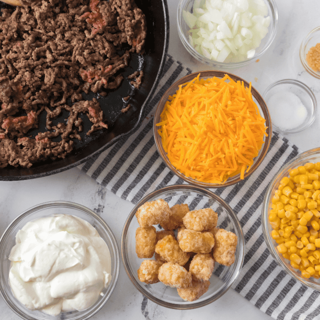 Ingredients for air fryer cowboy casserole: ground beef, onion, corn, cheddar, sour cream, and tater tots